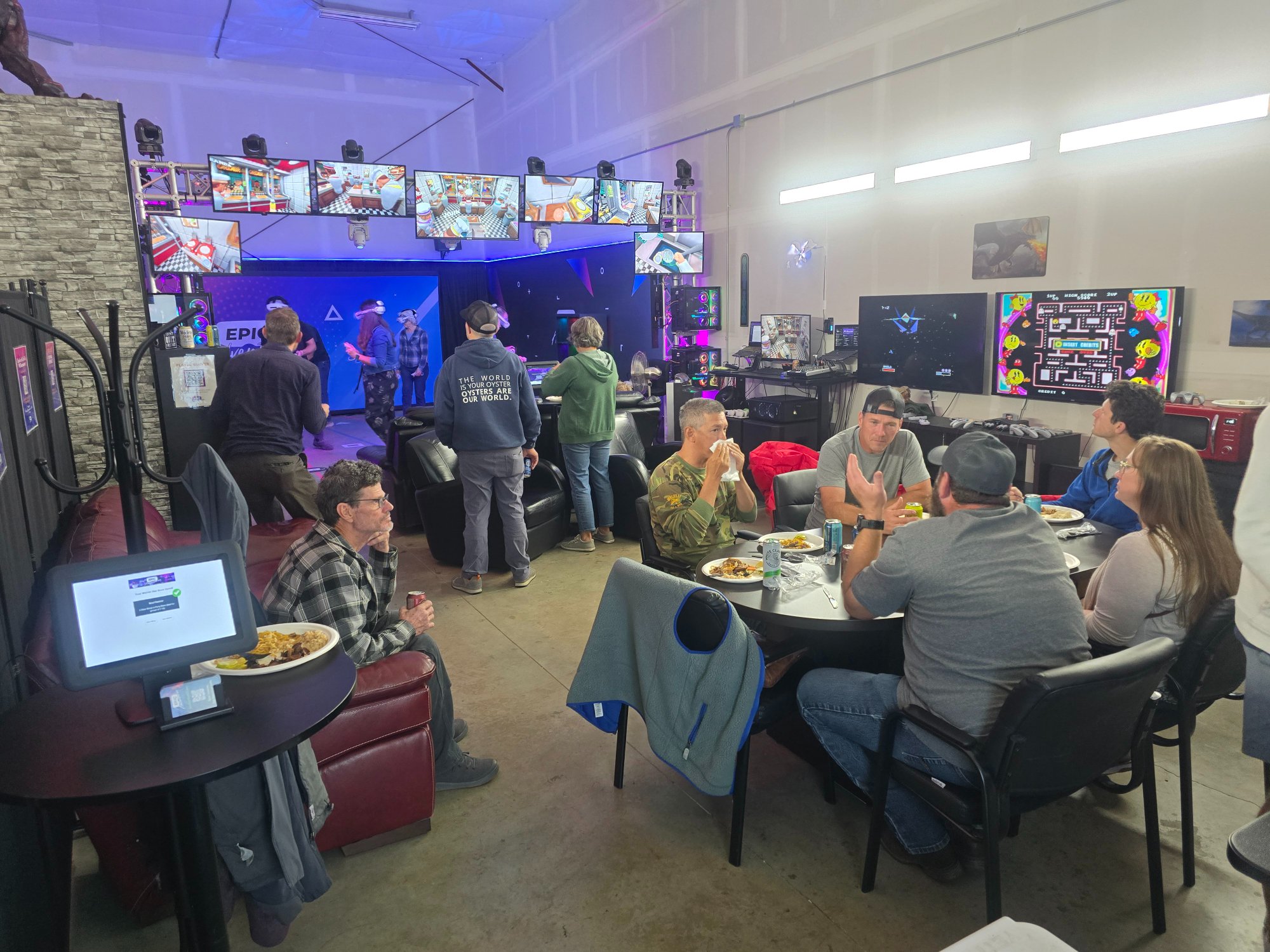 Corporate event at Epic Adventures showing employees eating catered food at dining tables while others play VR and retro arcade games in the background