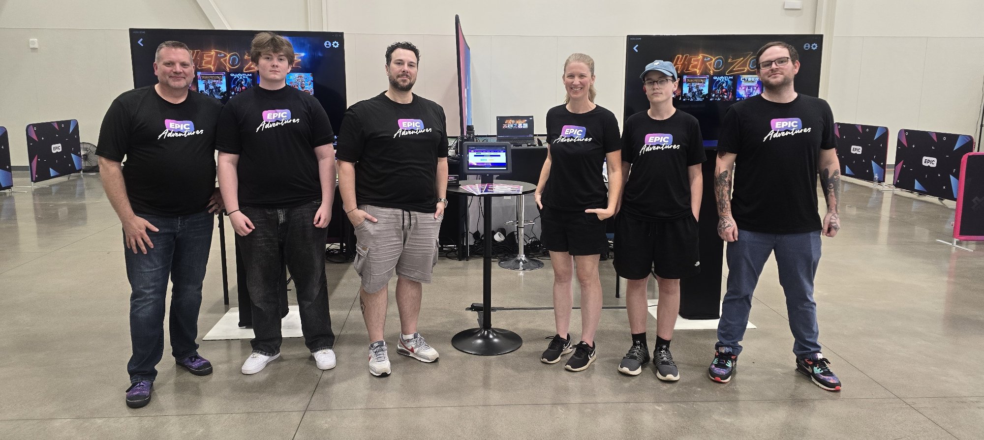 Epic Adventures VR team of six crew members in branded shirts standing in front of a dual mobile arena setup at a convention center event