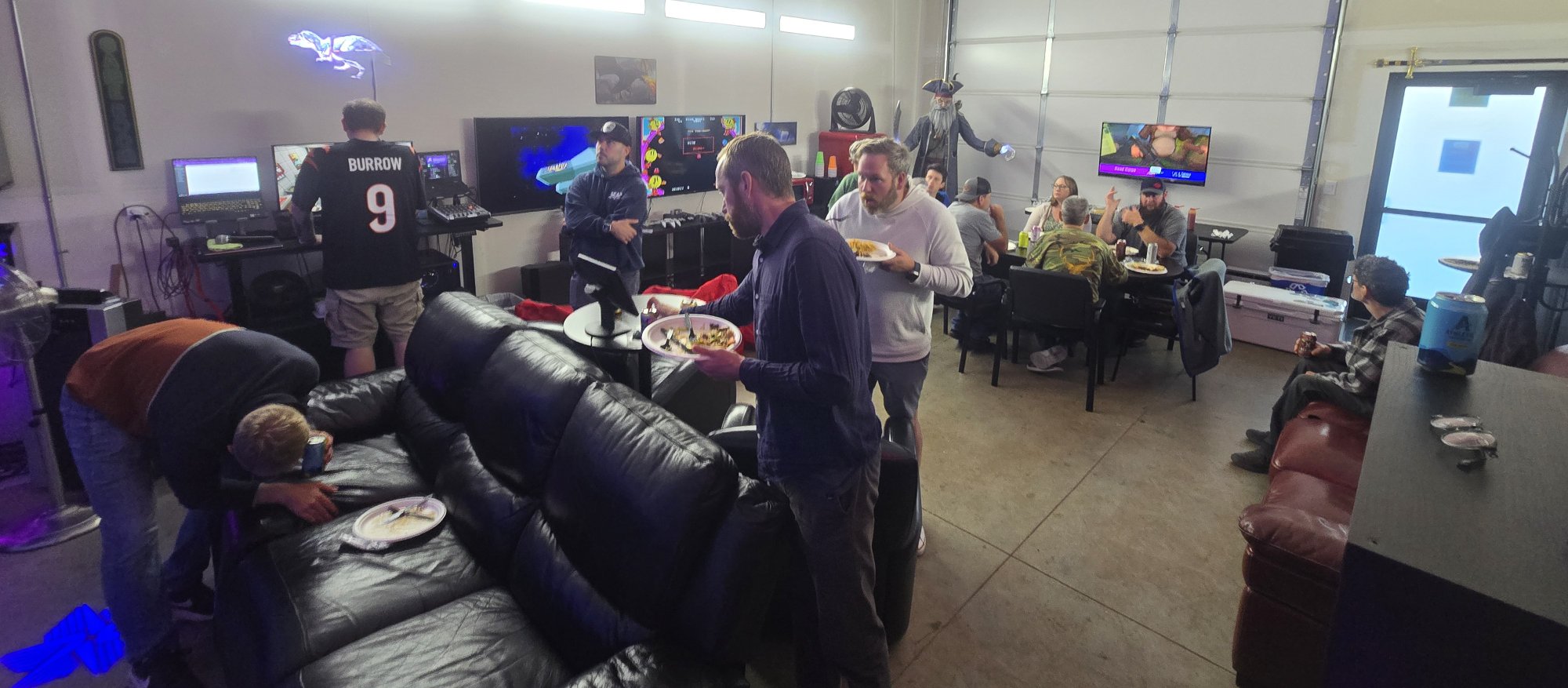 Guests socializing, eating food, and playing retro video games in the party space at Epic Adventures VR while others play in the arena